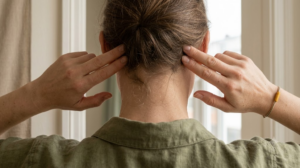Close view of a pair of hands pressing gently behind the ears of a person seen from behind.