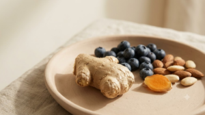 Fresh ginger root with blueberries and almonds on a shallow raw clay dish in soft daylight.