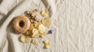 A glazed doughnut, sugar cubes and salted crisps on a plain surface.