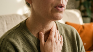 A person on a sofa breathing out slowly with one hand resting at the base of their throat.