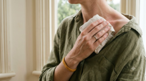 A person holding a cloth-wrapped ice cube against their collarbone in soft natural light.