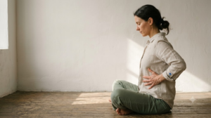 A person sitting on the floor breathing slowly with both hands resting on their ribs.