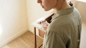 A person gargling a glass of water at a kitchen sink.
