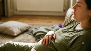 In profile on a worn rug, a person rests a warm hand low on their belly in raking late afternoon light.