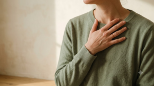 A person breathing out slowly with one hand resting flat against their collarbone in soft morning light.