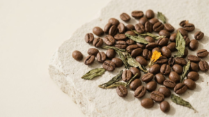 Roasted coffee beans and dried green tea leaves scattered across a pale stone slab.