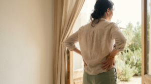 A person catching their breath after a walk with their hands resting on their hips in a bright doorway.