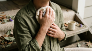 A close, warm photograph of a person pressing a cloth-wrapped ice pack to the base of their throat while sitting on a low step.