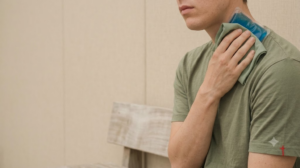 A person holding an ice pack against the side of their neck, photographed in soft natural light.