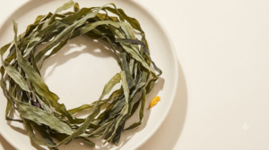 Dried sea kelp ribbons and pieces of dulse arranged in a loose ring on an unglazed ceramic plate.