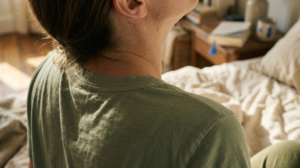 A close, warm over-the-shoulder photograph of a person singing out loud with their head tipped back among rumpled bed linen.