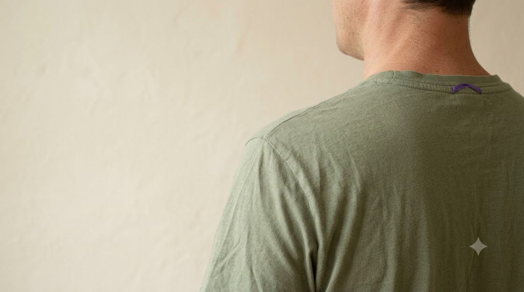 An over the shoulder view with the face turned away against a plain plastered wall, a person singing out steadily with their chest lifted.