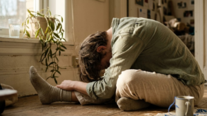 A person sitting cross-legged in a slow yoga forward fold beside a sunlit windowsill.