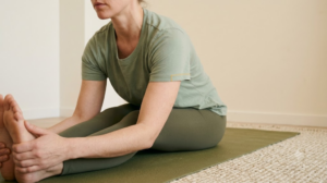 A person in a seated forward fold on a yoga mat in a calm, softly lit room.