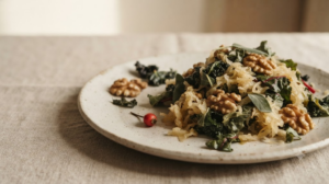 Close still life of a heap of sauerkraut with shelled walnuts and dark leafy greens behind it on an unglazed ceramic plate.