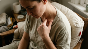 Seen from just above, a person presses a thumb into the hollow above their collarbone in a deep armchair.