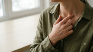 A person in an olive linen shirt presses a fingertip into the hollow above their collarbone.