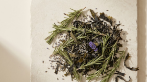 Rosemary sprigs, dried seaweed and lavender buds gathered in a loose mound on a pale stone slab.