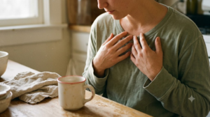 Both hands resting on a chest with shoulders dropping, at a kitchen table in warm late afternoon light.