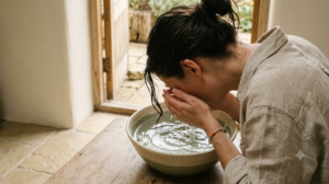 A person lowers their face towards a bowl of cold water in a calm, softly lit room.