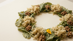 A still life of loose sauerkraut, leafy greens and walnuts arranged in a wide ring on soft cream paper.
